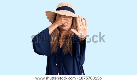 Middle age hispanic woman wearing summer hat covering eyes with hands and doing stop gesture with sad and fear expression. embarrassed and negative concept. 