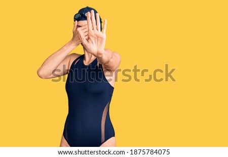 Young beautiful hispanic woman wearing swimwear and swimmer glasses covering eyes with hands and doing stop gesture with sad and fear expression. embarrassed and negative concept. 
