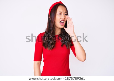 Young beautiful chinese girl wearing casual clothes shouting and screaming loud to side with hand on mouth. communication concept. 