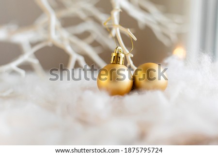 Two golden christmas baubles in dreamy white landscape. White tree branches blurred in the backgound.