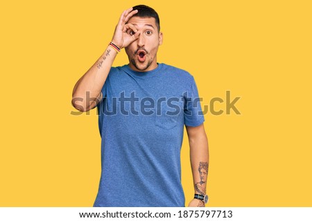 Handsome man with tattoos wearing casual clothes doing ok gesture shocked with surprised face, eye looking through fingers. unbelieving expression. 