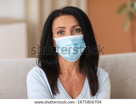 Protection Concept. Portrait of adult brunette woman wearing hygienic disposable face mask to prevent infection, airborne respiratory illness such as flu, 2019-nCoV coronavirus, looking at camera