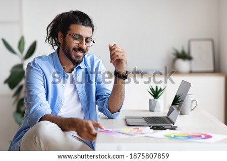 Arab Man Graphic Designer Working With Color Swatches And Laptop At Home Office, Sitting At Desk And Checking Colour Samples For New Project, Enjoying Self-Employment And Remote Work, Free Space