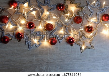 Christmas and New Year composition from christmas decorations, garland of yellow led lights and red shiny, sparkling and matte balls on light oak wood textured surface with copy space