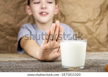 The boy looks at a glass of milk and shows a stop sign with his hand. A health problem related to dairy products.
