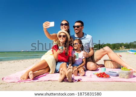 family, leisure and people concept - father, mother and two little daughters taking selfie with smartphone on summer beach