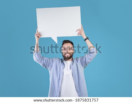 Happy millennial man holding blank speech bubble above his head over blue studio background, copy space. Handsome young guy with empty word cloud, mockup for design