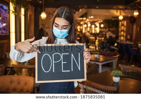 Woman coffee shop owner with face mask opens after lockdown quarantine. Open. barista, waitress woman wearing protection face mask turning open sign board on glass door in modern cafe coffee shop