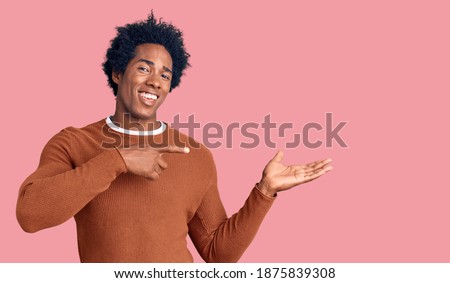 Handsome african american man with afro hair wearing casual clothes amazed and smiling to the camera while presenting with hand and pointing with finger. 