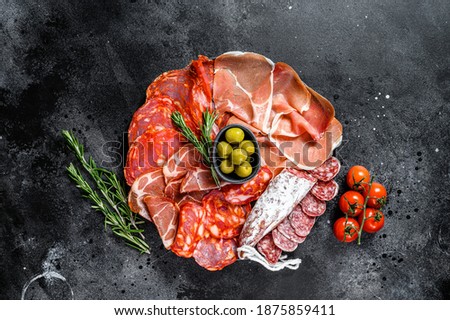 Cured meat platter of traditional Spanish tapas. Chorizo, jamon serrano, lomo and fuet. Black background. Top view. Royalty-Free Stock Photo #1875859411