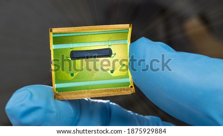 Close-up of flex circuit board in human fingers detail on dark background. Hand in blue glove holding green plastic flexible PCB for parallel transmission of digital data signals in LCD devices. Tech.