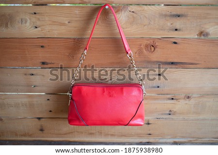 A red bag is hanging on a brown wooden wall.