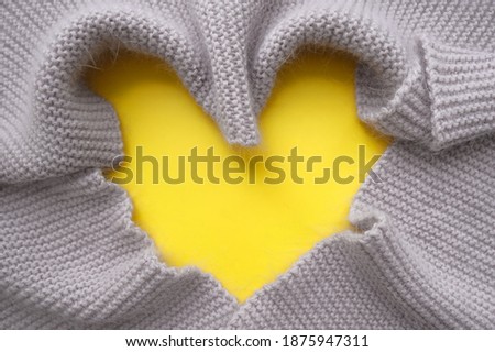 Gray knitted scarf lies in the shape of  heart on yellow .  Symbolize warmth, love and tenderness.  Valentine's Day concept. Trendy Color 2021. Copy space