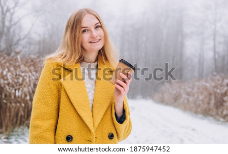 Happy young Woman holds paper coffee cup over nature background, trendy color of year 2021 - illuminatiing yellow. Take away or delivery concept. Copy space.
