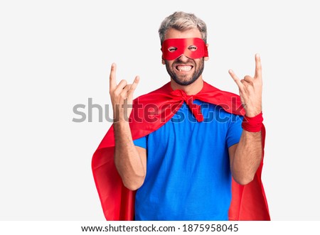 Young blond man wearing super hero custome shouting with crazy expression doing rock symbol with hands up. music star. heavy concept. 