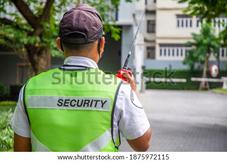 The back of a security guard is using a radio.