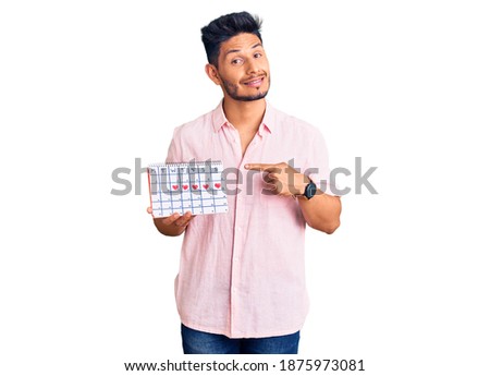 Handsome latin american young man holding heart calendar smiling happy pointing with hand and finger 