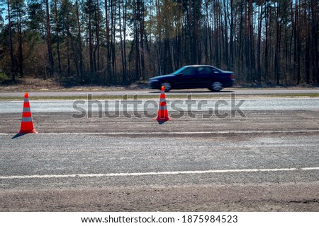 Road cones stands on the road against the background of a fast-moving car. Safety cones or safety pylon on the asphalt set up to direct traffic