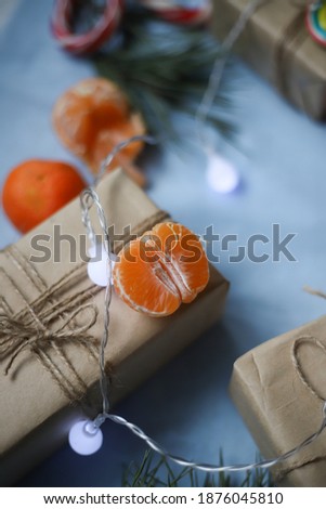 New Year's picture on which gifts in craft paper and twine are decorated with multi-colored candies and Christmas tree branches with sweet tangerines and a garland on a blue background