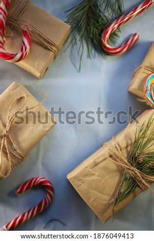 New Year's picture on which gifts in craft paper and twine are decorated with multi-colored candies and Christmas tree branches on a blue background