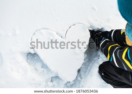 The boy is make a shape of heart on the snow. Winter.