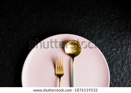 A fork and spoon on top of a pink plate isolated on a black background. Modern food.