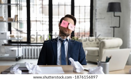 Tired sleepy businessman with stickers, adhesive notes on eyes sleeping at workplace, sitting at work desk in office, unproductive lazy employee executive dozing, working on difficult project Royalty-Free Stock Photo #1876156897
