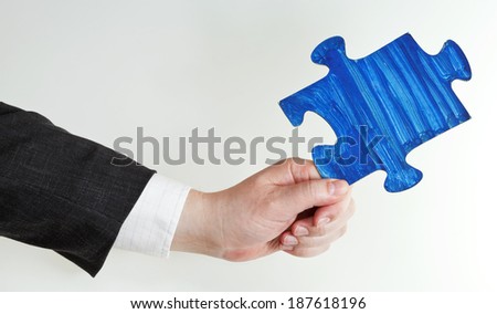 blue painted puzzle piece in male hand on grey background