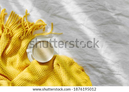 Bedding with a yellow knitted plaid and cup of coffee . Cozy background with copy space. Hygge concept.