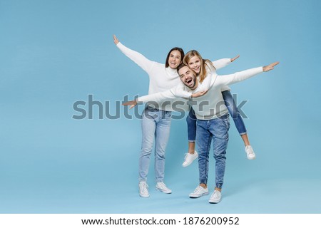 Full length of excited young parents mom dad with child kid daughter teen girl in sweaters giving piggyback ride to joyful, sitting on back isolated on blue background. Family day parenthood concept