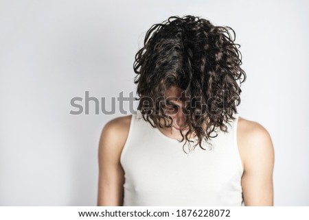 A teenage boy with long curly hair on a light background lowered his head, he seems to apologize for his misdeeds to parents, asks to understand him and help to solve teenage problems. Copy space Royalty-Free Stock Photo #1876228072