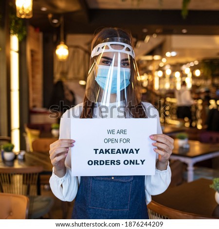 Barista holding  sign we’re open for takeaway orders only in front of restaurant. Social distancing concept when coronavirus is outbreak in city. 