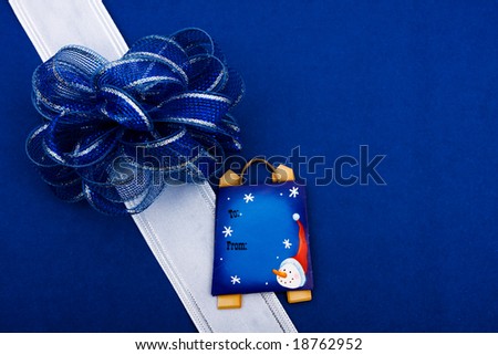White ribbon and blue bow with blank gift tag on blue background making a present, present