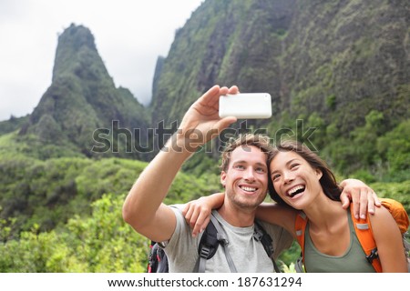 Couple taking selfie photo with smart phone hiking on Hawaii. Woman and man hiker taking photo with smart phone camera. Healthy lifestyle from Iao Valley State Park, Wailuku, Maui, Hawaii, USA.