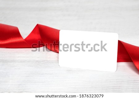 Empty card for advertising, text, discounts on a white wooden background with a red festive ribbon.