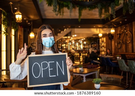 Small business owner with face mask holding the sign for the reopening of the place after the quarantine due to covid-19. Woman with protective mask holding sign we are open, support local business.