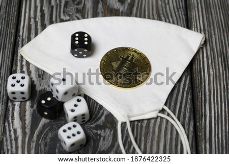 Bitcoin lies on a medical mask. Dice are scattered nearby. On pine boards.