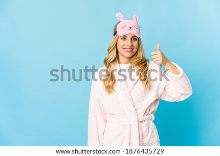 Young blonde caucasian woman wearing a pajama smiling and raising thumb up