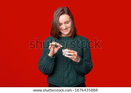 Young pretty girl is opening a small silver gift over red background.