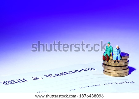 Conceptual image of miniature a figure elderly couple sat on coins at the side of a last will and testament document, Royalty-Free Stock Photo #1876438096