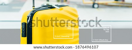 The bright and stylish yellow cabin size suitcase in the airport with gray background, holiday concept. Easy travel with little baggage, trendy colors of 2021