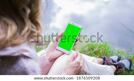 The smartphone in the hands of a young woman in park