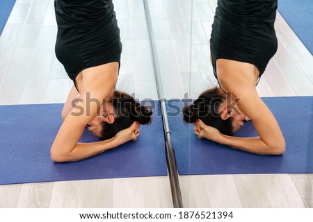 Young attractive yogi woman practicing yoga concept, doing headstand pose, working out, wearing sportswear