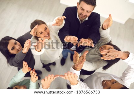 High angle of group of happy smiling young diverse people standing in office and raising hands up in air. Concept of business team aspiring for success and trying to achieve common goal together