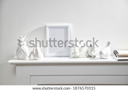 Figurines of a polar bear, pineapple, pears, an angel, a bullfinch bird, and a white photo frame with empty space on a white fireplace console. Copy space. Place for text