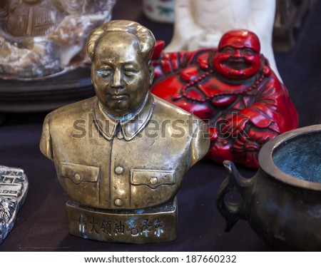 Bust of China's former Chairman Mao Zedong and red Laughing Buddha figurine at background. Still life at flea market in Paris (France). Idea of the contrasts in life.