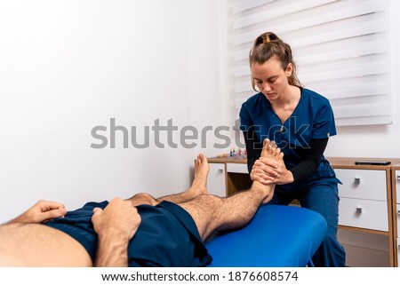 Stock photo of physiotherapist giving feet massage to patient lying in stretcher.