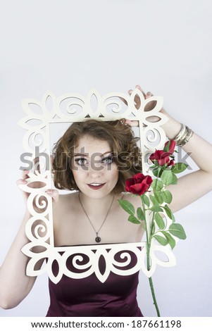 Beautiful young woman wearing strapless burgundy dress posing with white picture frame and red roses.