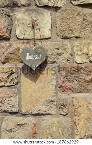 Stone wall with wooden Heart shape with text bonheur which is french for happiness