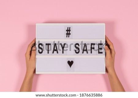 Hands holding lightbox with message Stay Safe on pink background. isolated. Healthcare, social distancing concept. Top view